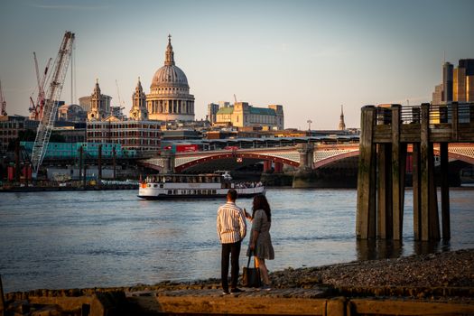 A couple standing by the Thames in London, overlooking St Paul's Cathedral during sunset with cityscape backdrop.