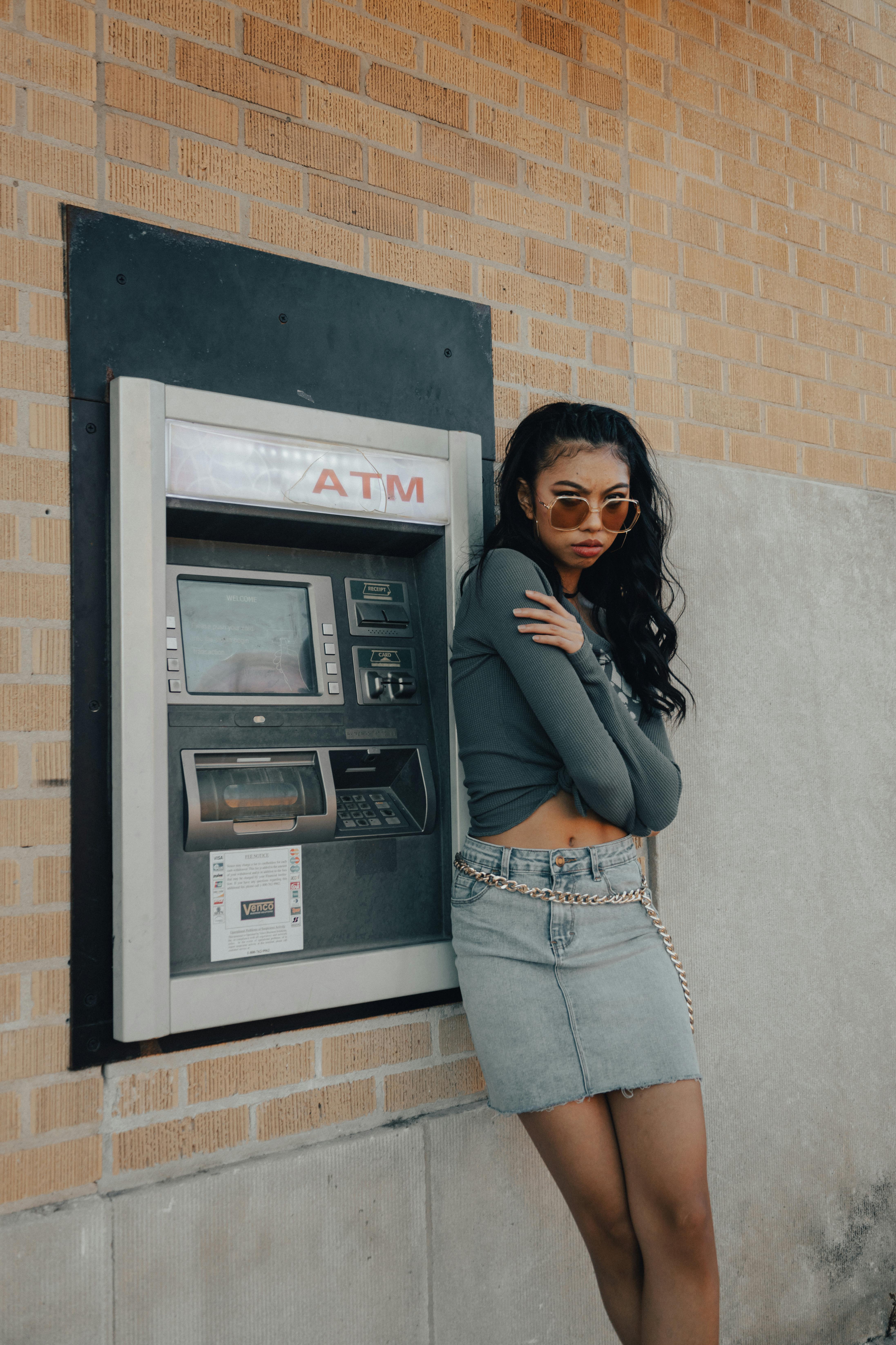 a woman leaning against a wall with an atm machine