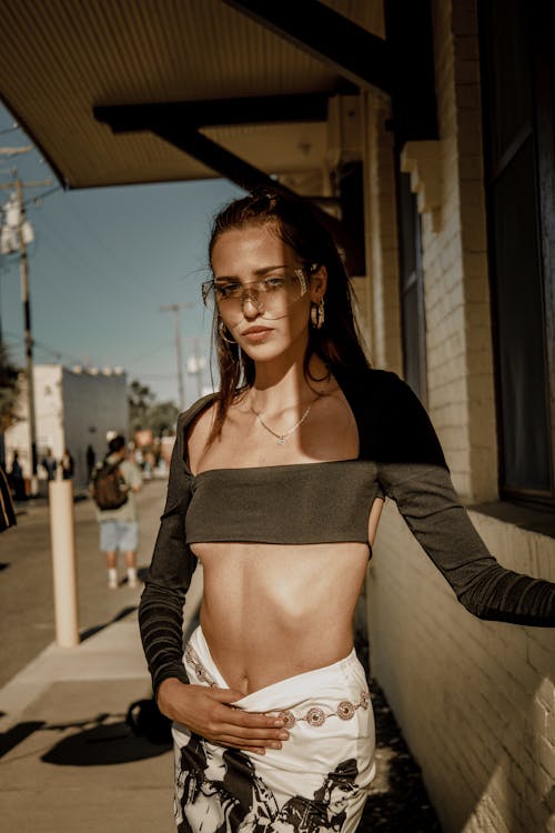 A woman in a crop top and pants standing on a sidewalk
