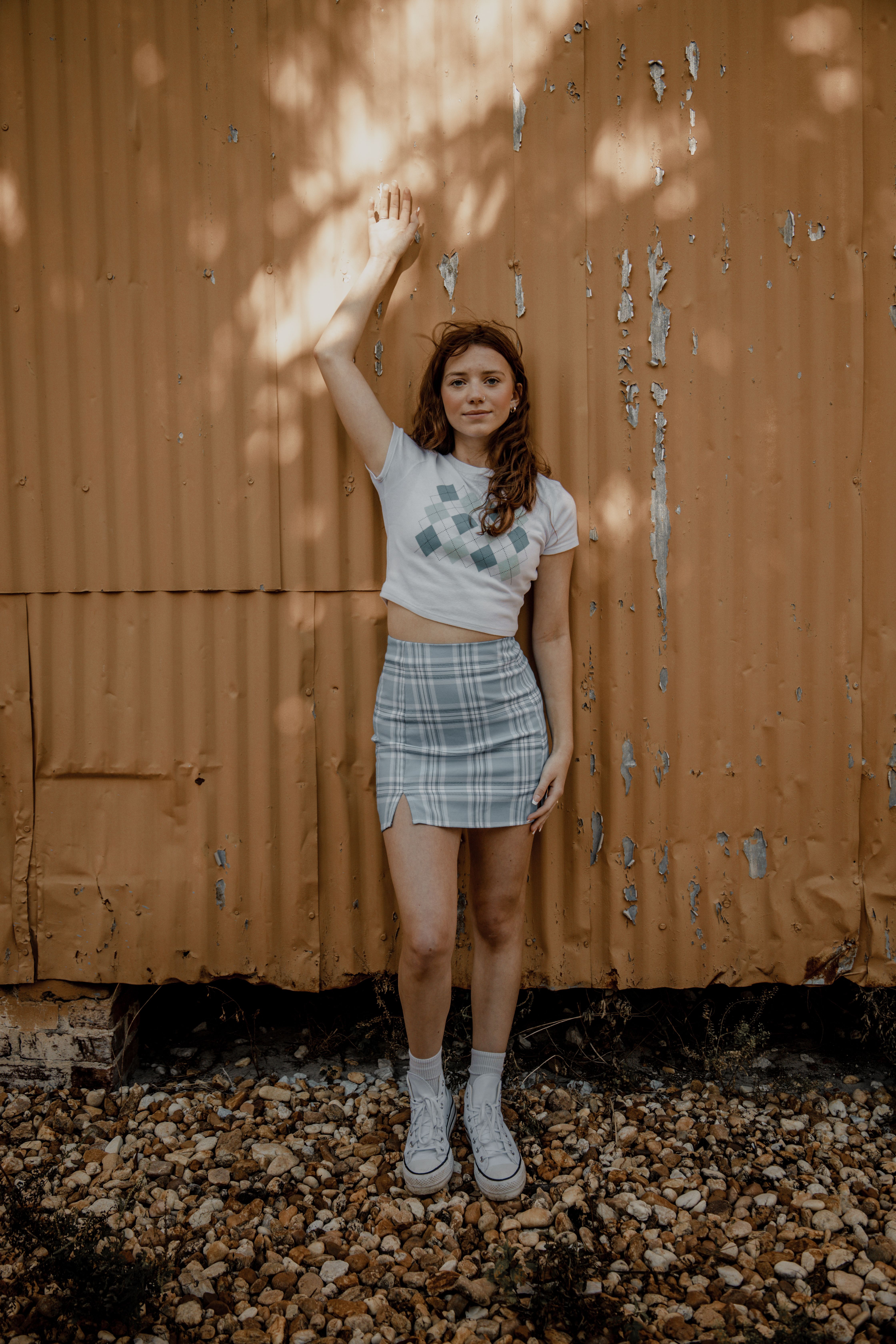 A girl standing in front of a rusty wall wearing a white t shirt and ...