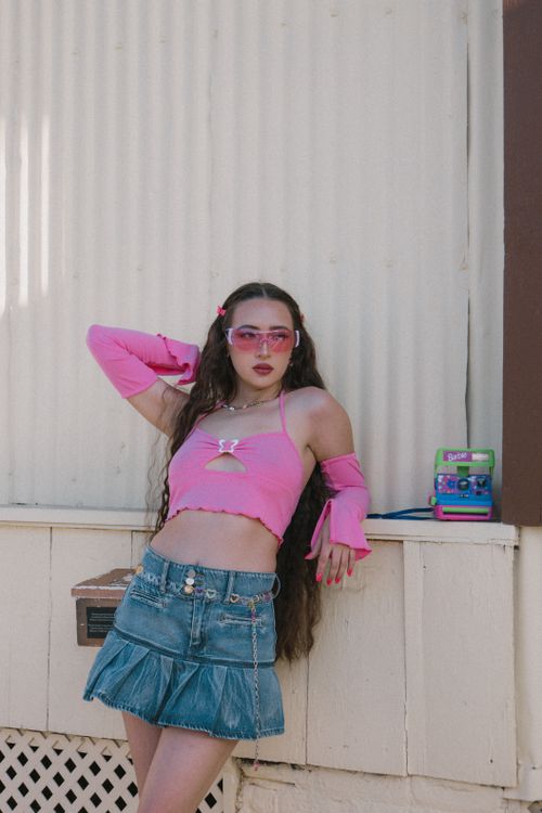 Free Stylish young woman poses confidently in a vibrant pink top and denim skirt outdoors. Stock Photo