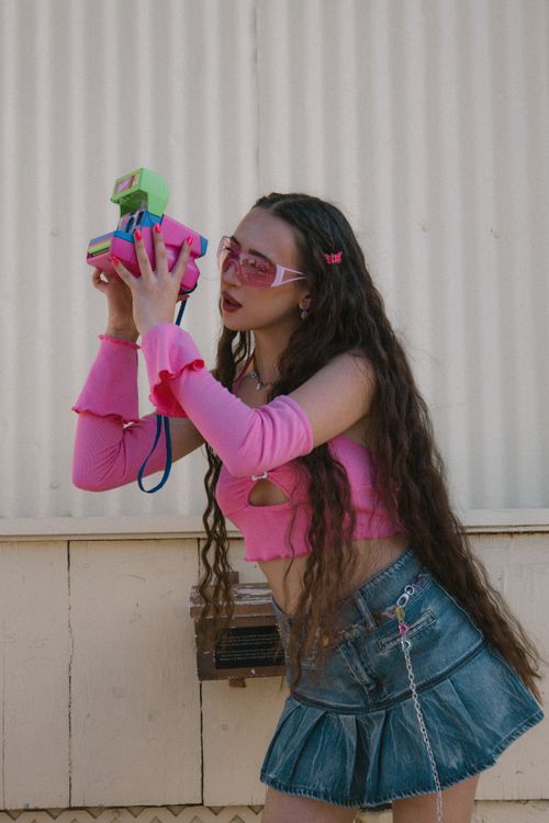 Free Stylish young woman in pink outfit using a colorful retro camera outdoors. Stock Photo