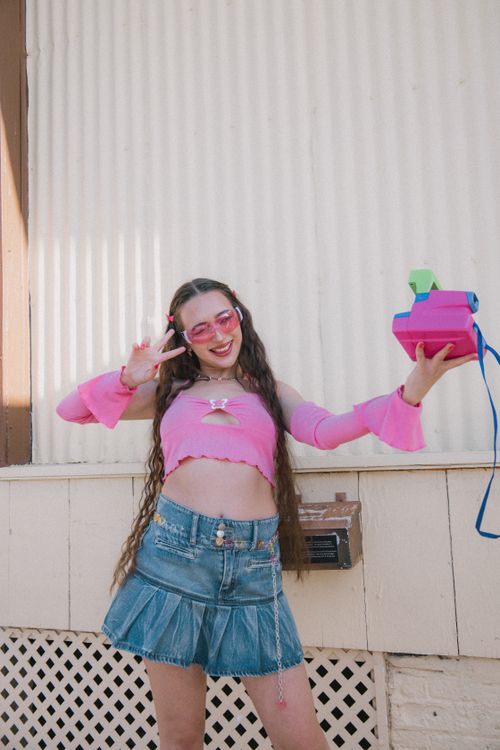 Free Trendy young woman in pink and denim posing outdoors with a colorful prop camera, exuding youthful energy. Stock Photo