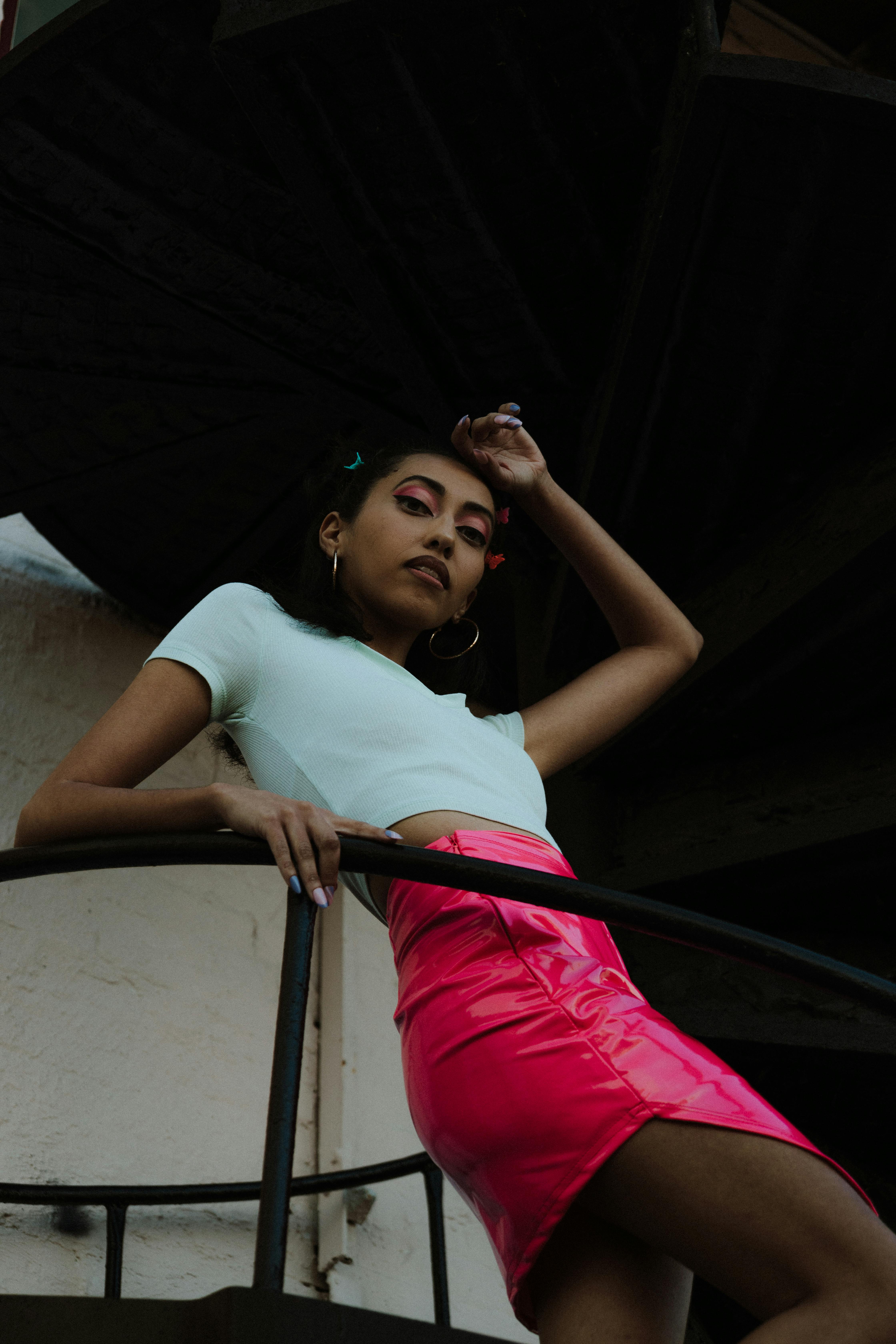 a woman in a pink skirt and white top is posing on a railing