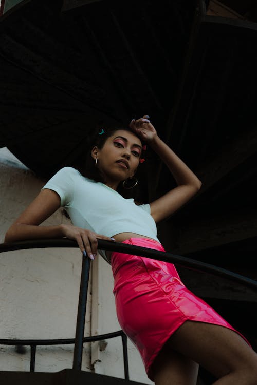 A woman in a pink skirt and white top is posing on a railing