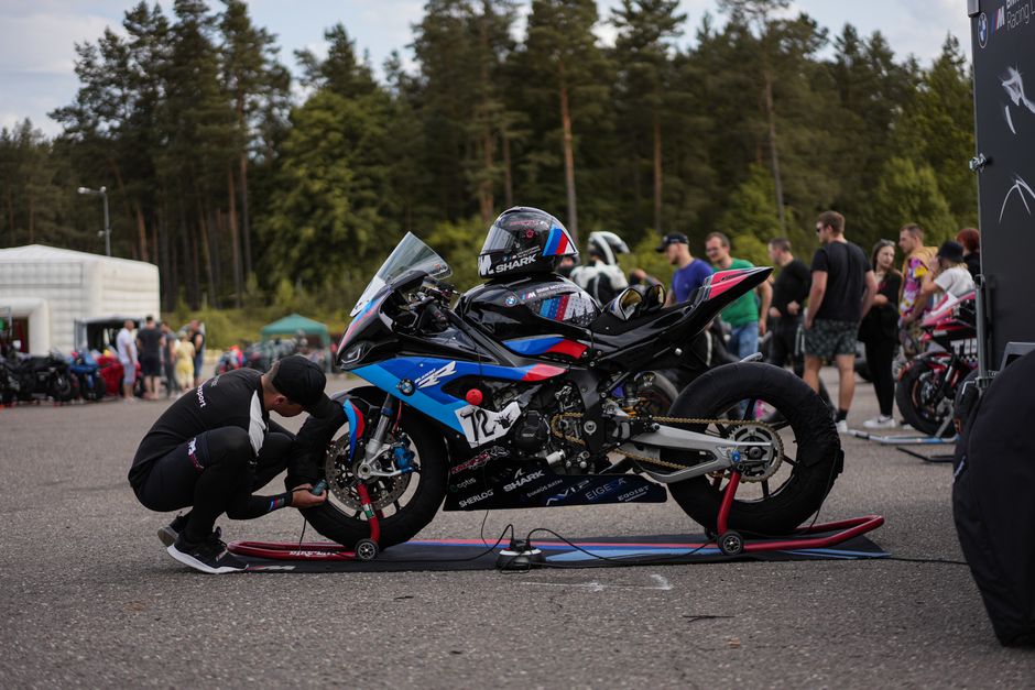 A man prepares a racing motorcycle at an outdoor event with spectators.