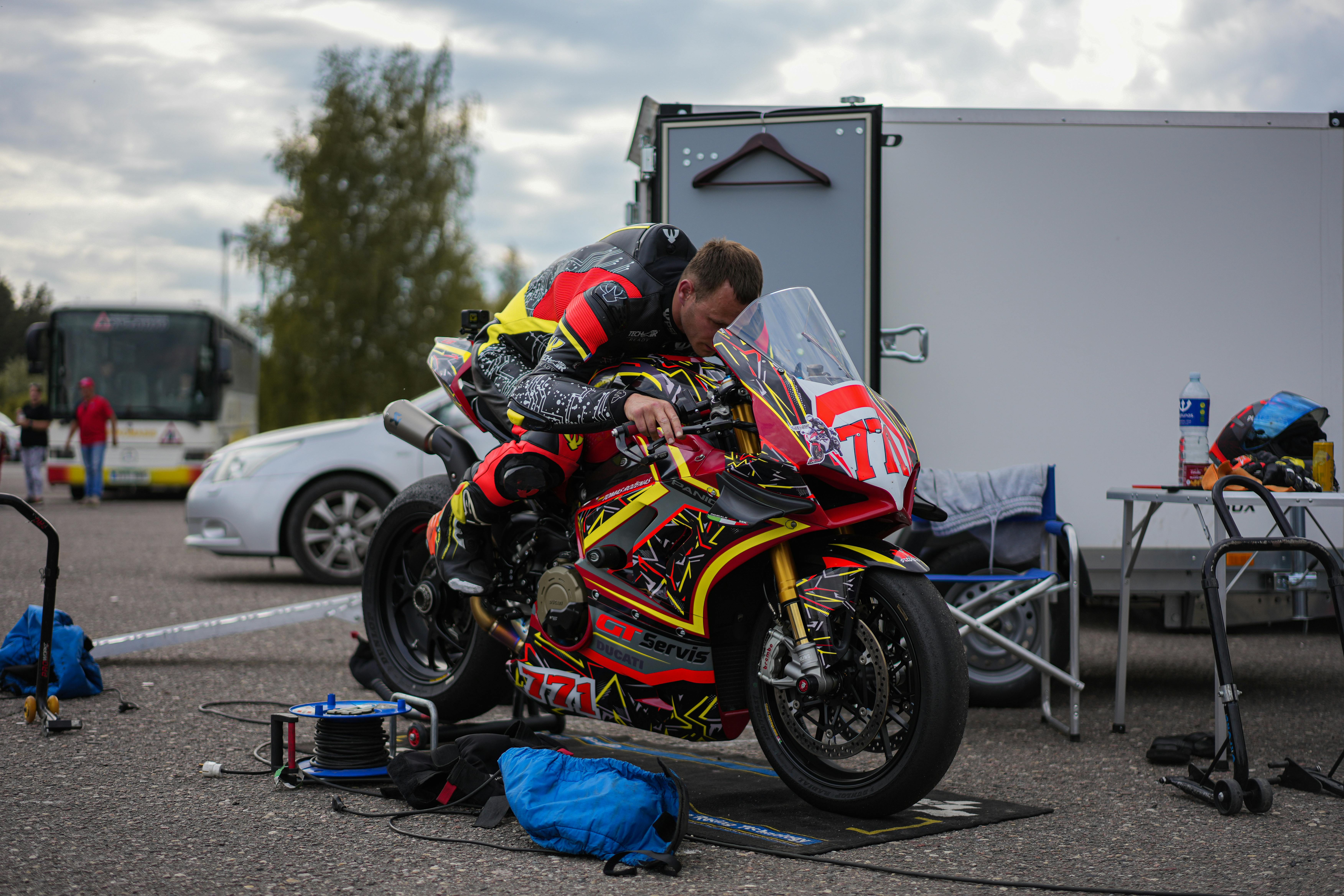 Motorcyclist adjusts colorful racing bike for an upcoming motorsport event outdoors.