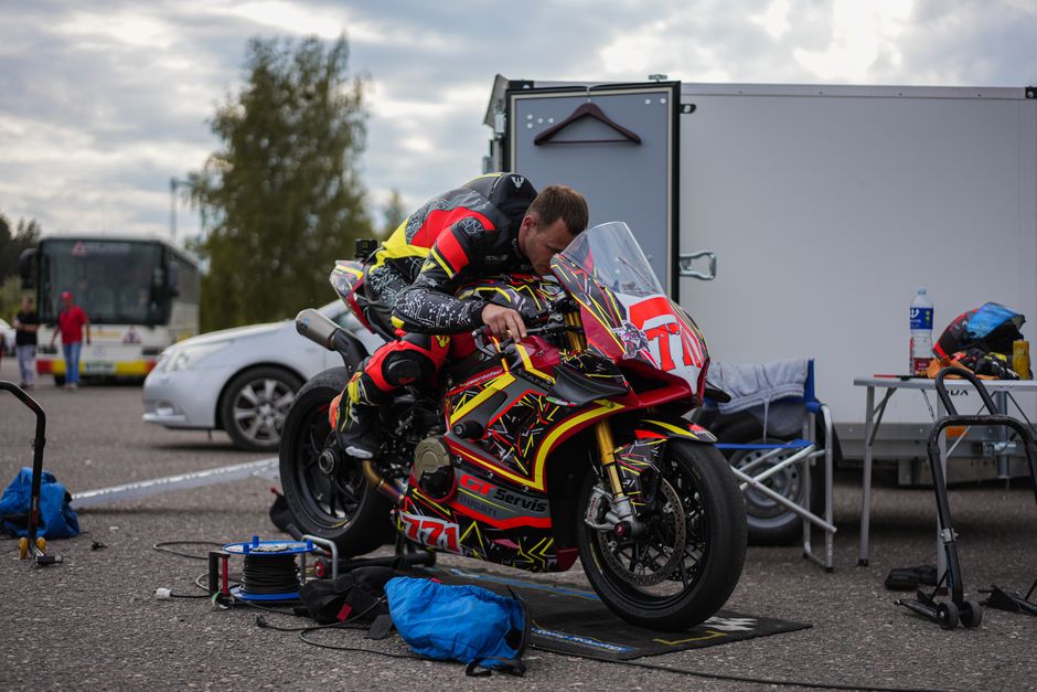 Motorcyclist adjusts colorful racing bike for an upcoming motorsport event outdoors.