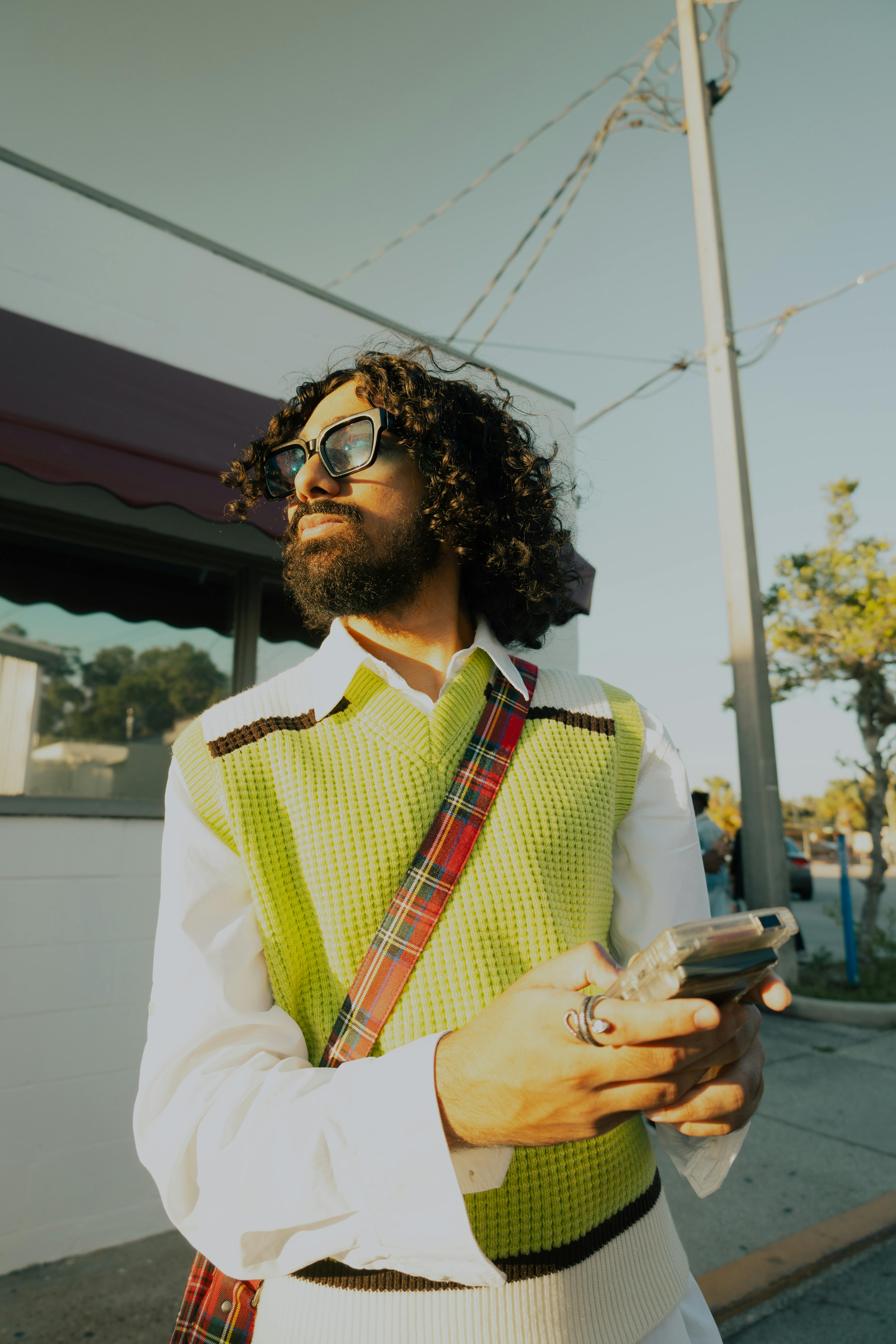 Free A fashionable man with curly hair and sunglasses enjoying the sunny street. Stock Photo