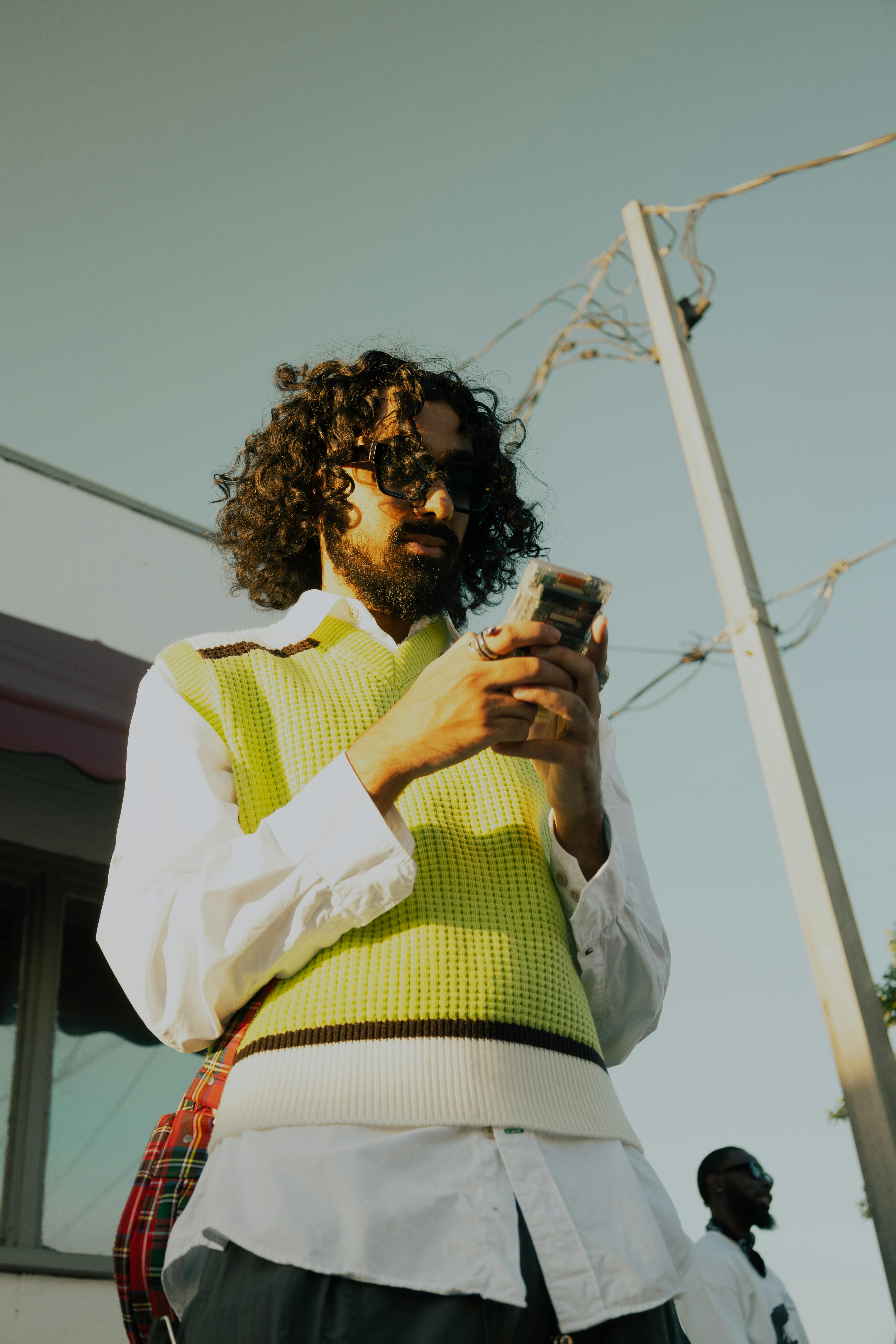 Free Urban scene of a fashionable man with curly hair checking his phone outdoors during sunset. Stock Photo