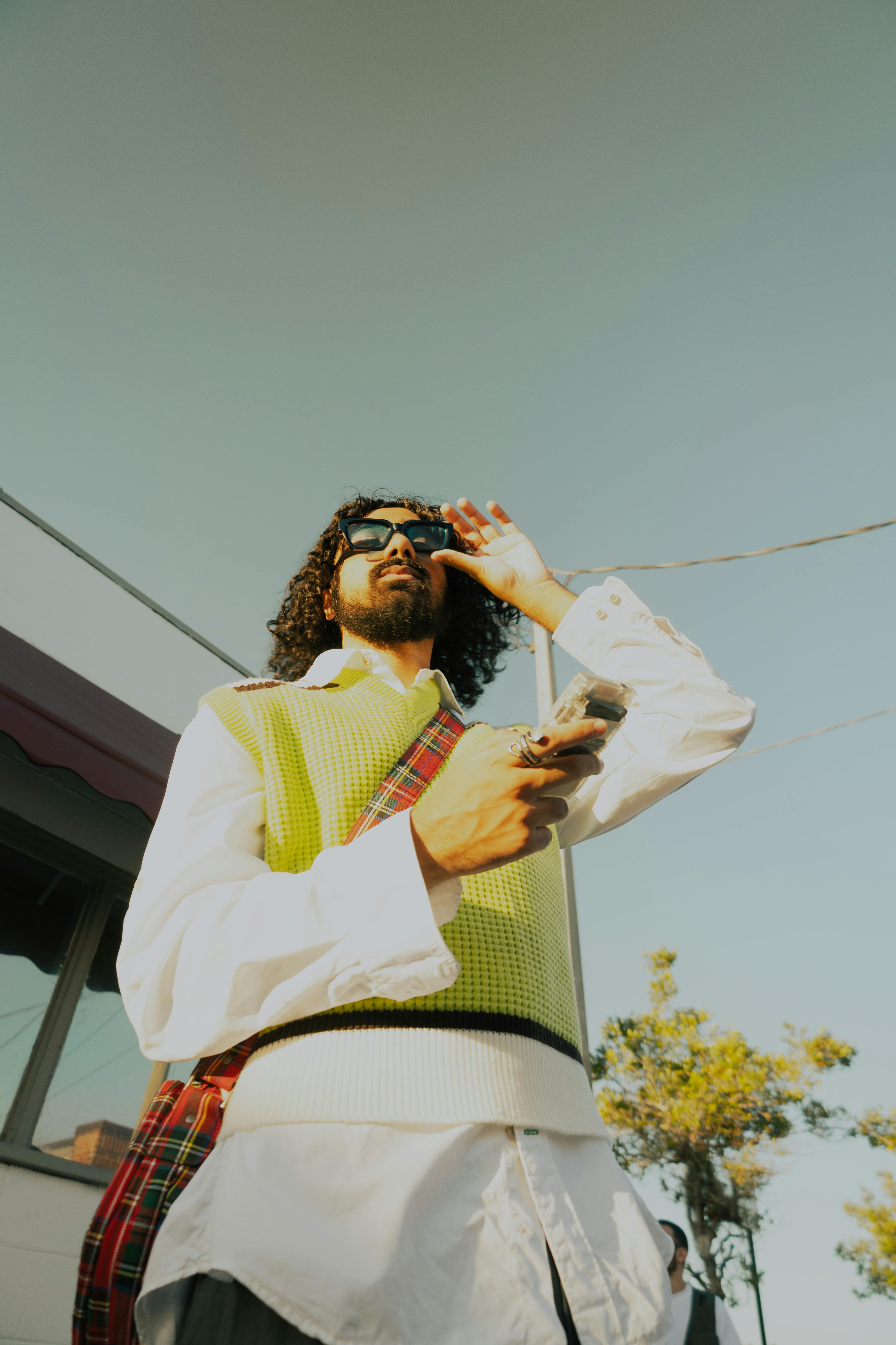 a man in a vest and sunglasses is holding a cell phone