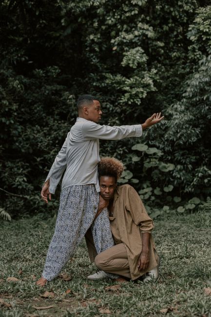 Two men pose artistically in a lush green outdoor setting, capturing a moment of expression and style.