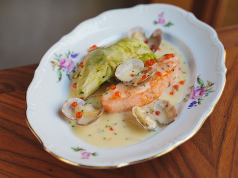 Close-up of a gourmet salmon and clam dish with cream sauce on a floral plate.