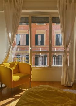 A bright interior featuring a comfortable yellow armchair, large windows, and white curtains.