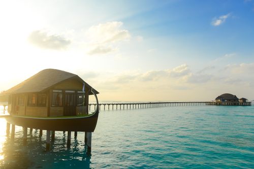 Free Overwater bungalow on a serene ocean backdrop at sunrise, perfect for a tropical escape. Stock Photo