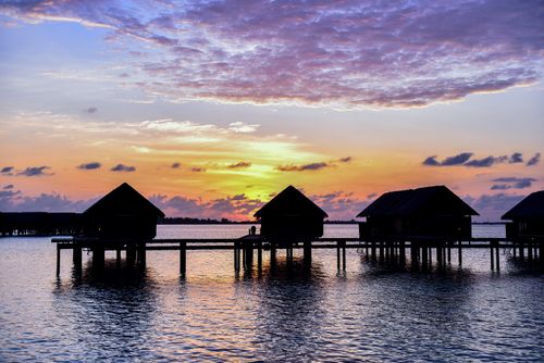 Free Overwater bungalows silhouetted against a vibrant sunset sky by the sea. Stock Photo