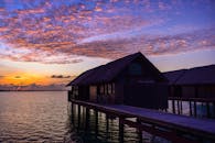 一座风景如画的水上平房，倒映在平静的海面上，与天空中绚烂的云霞和壮丽的日落交相辉映