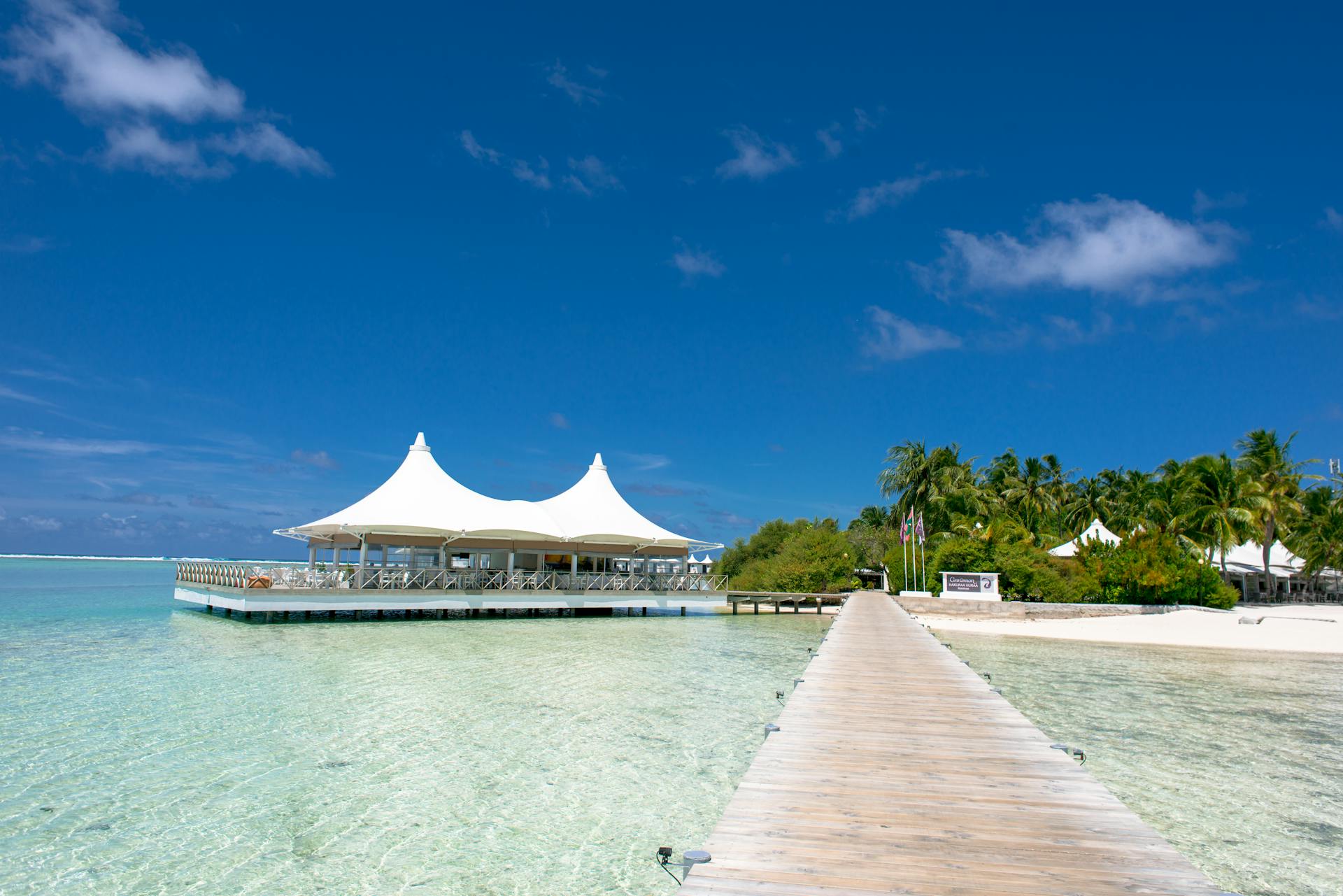 Scenic view of a tropical beach resort featuring a wooden pier, azure waters, and a clear blue sky.