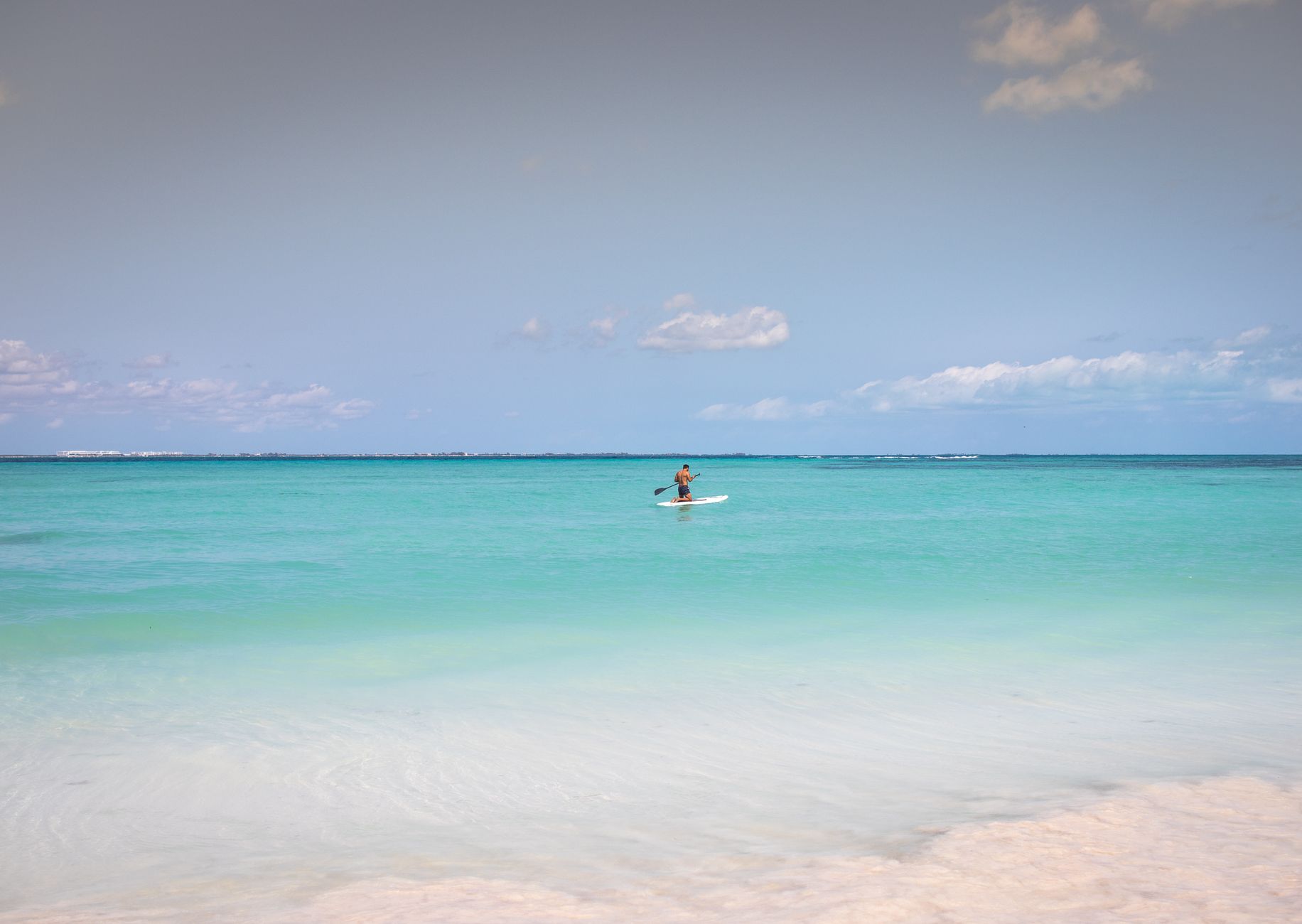 A man enjoys paddleboarding on the serene turquoise waters of Cancún, México under a clear sky. (stock photo)