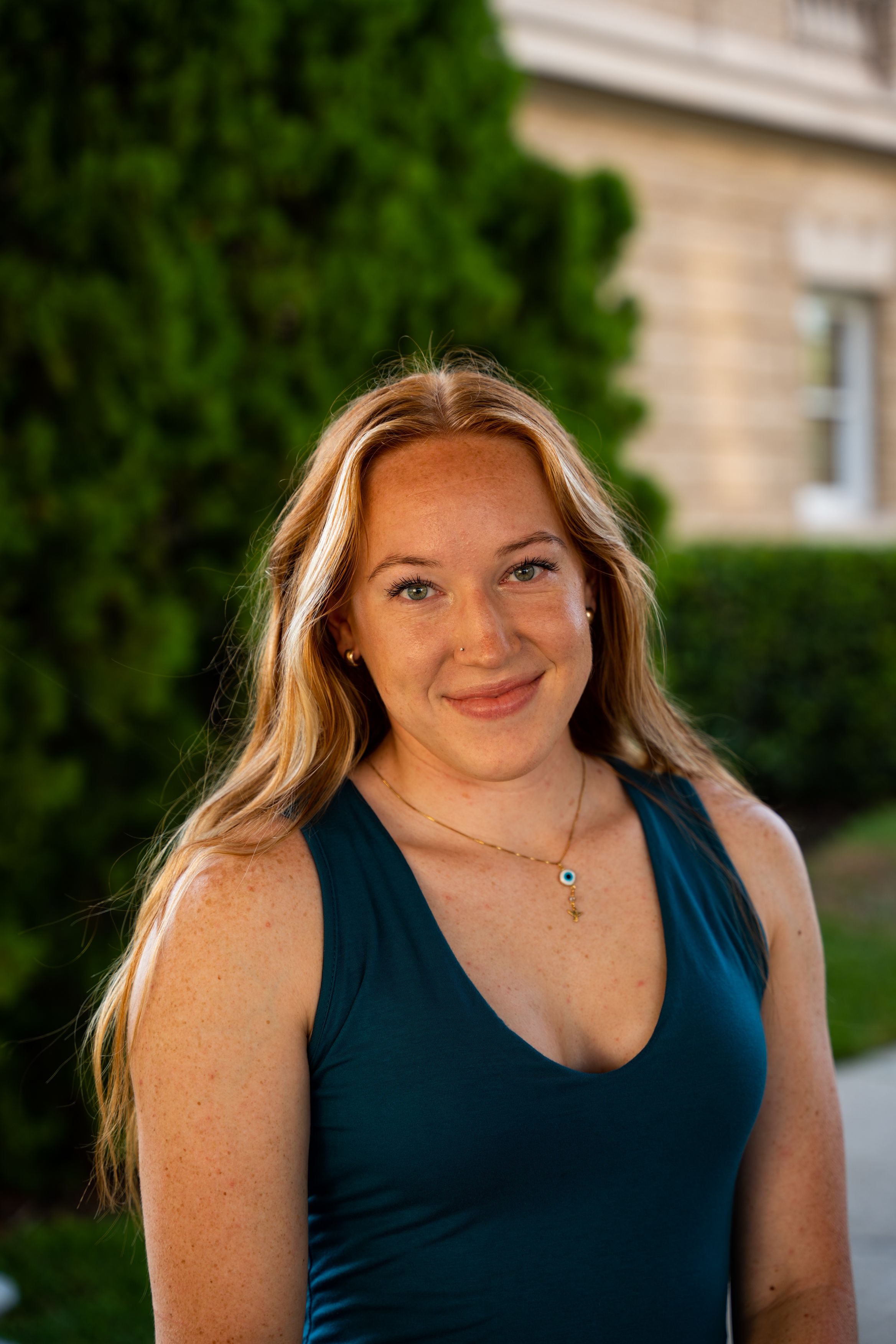 Portrait of a smiling woman in a blue dress standing outdoors with a blurred green background.
