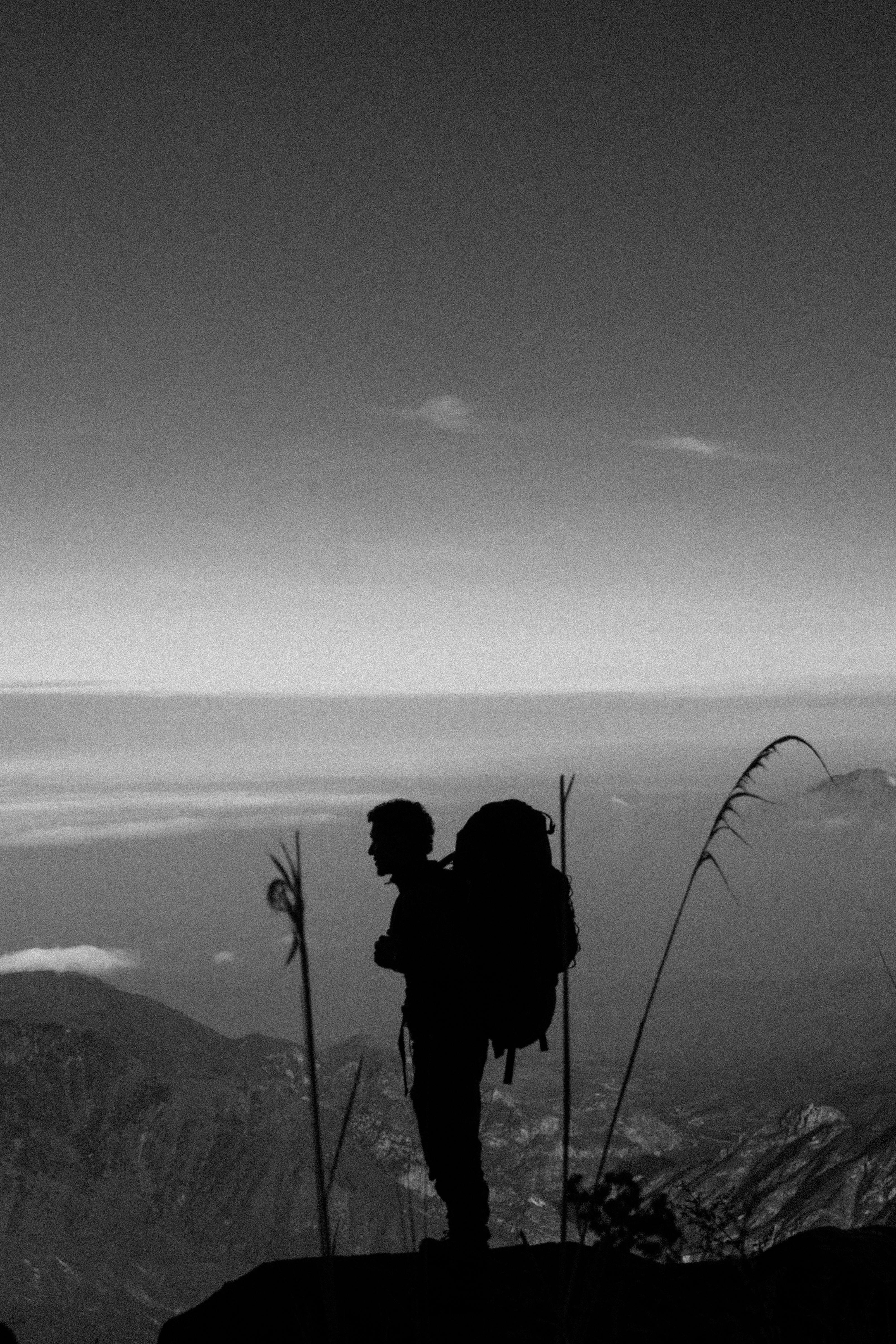 Black and white silhouette of a hiker with backpack standing on mountain peak.