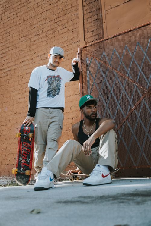 Free Two male skateboarders posing stylishly against an urban brick wall backdrop. Stock Photo