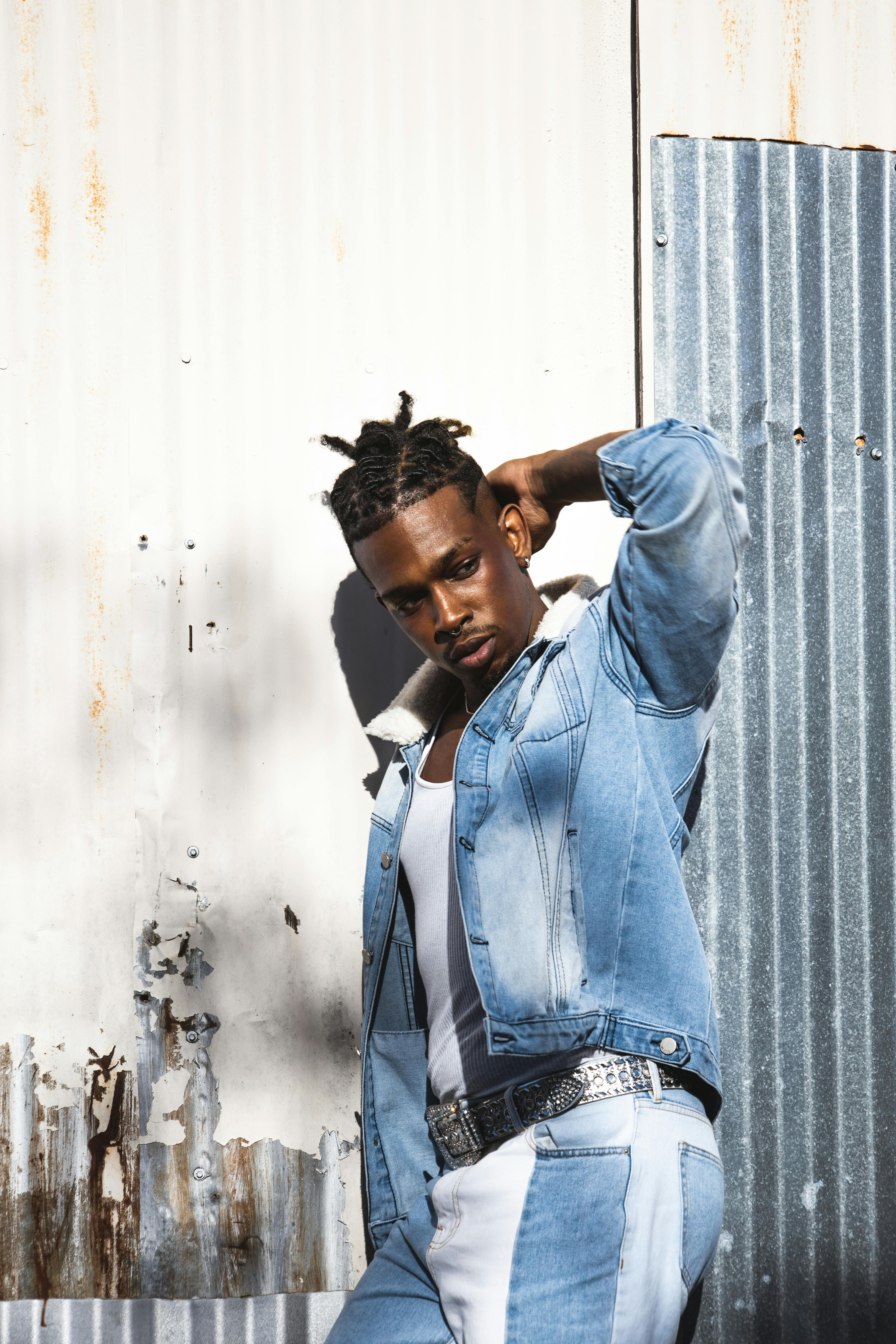 a young man in denim jacket leaning against a wall