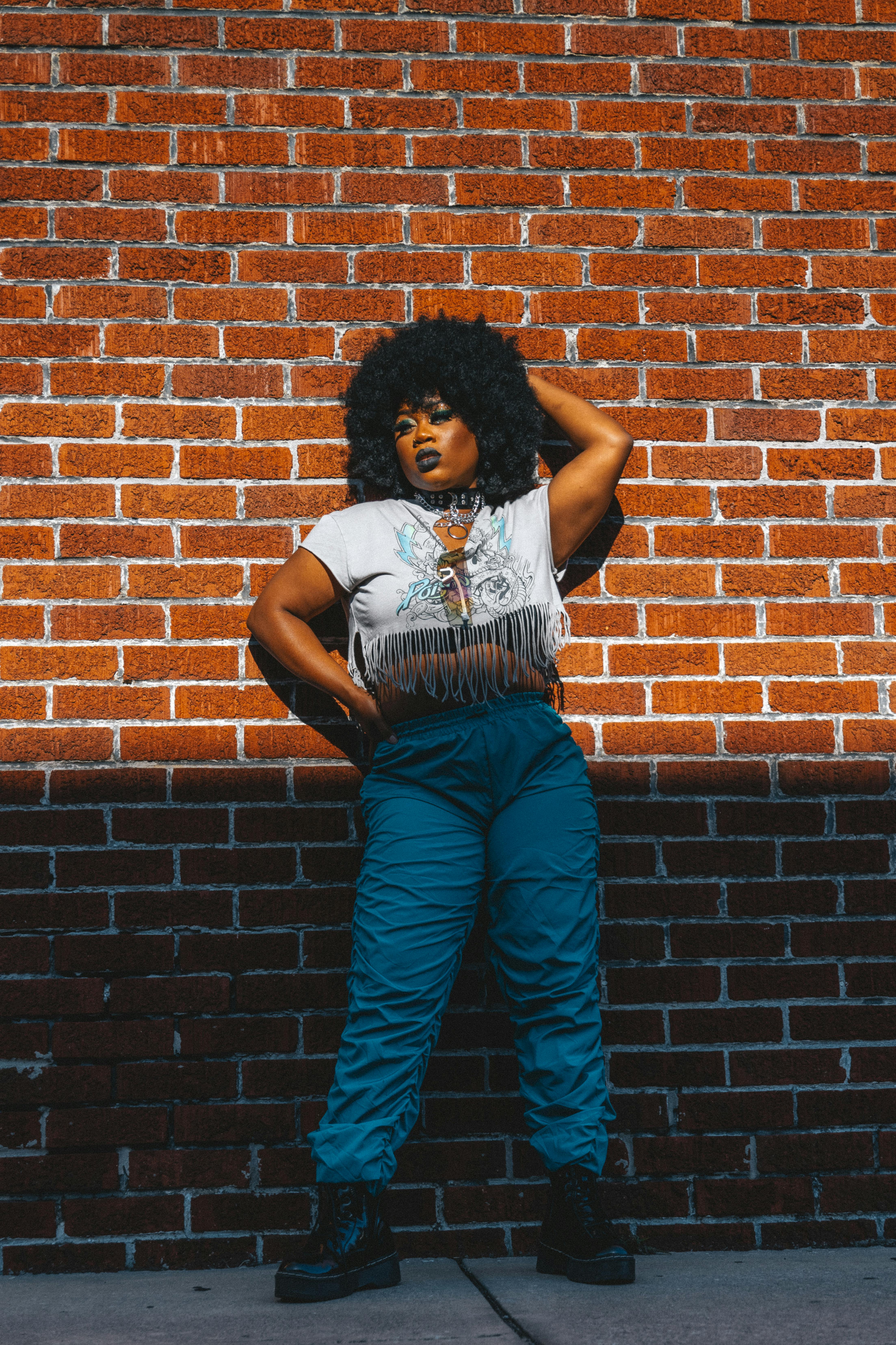 a woman leaning against a brick wall wearing blue pants