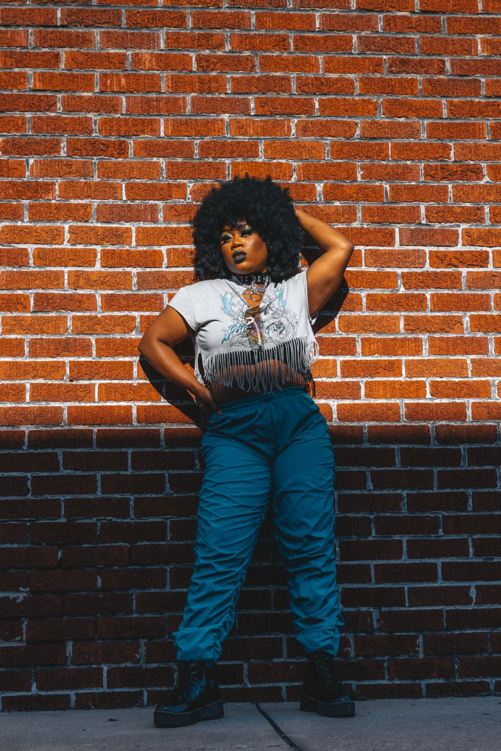A woman leaning against a brick wall wearing blue pants · Free Stock Photo
