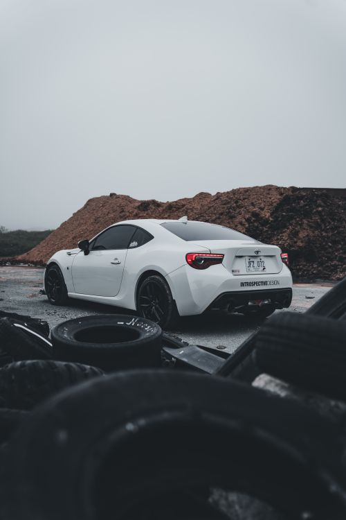 Free A white sports car parked outdoors behind tire stacks, showcasing modern automotive design. Stock Photo