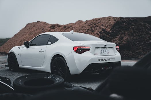 A modern white sports car parked outdoors against an industrial backdrop.