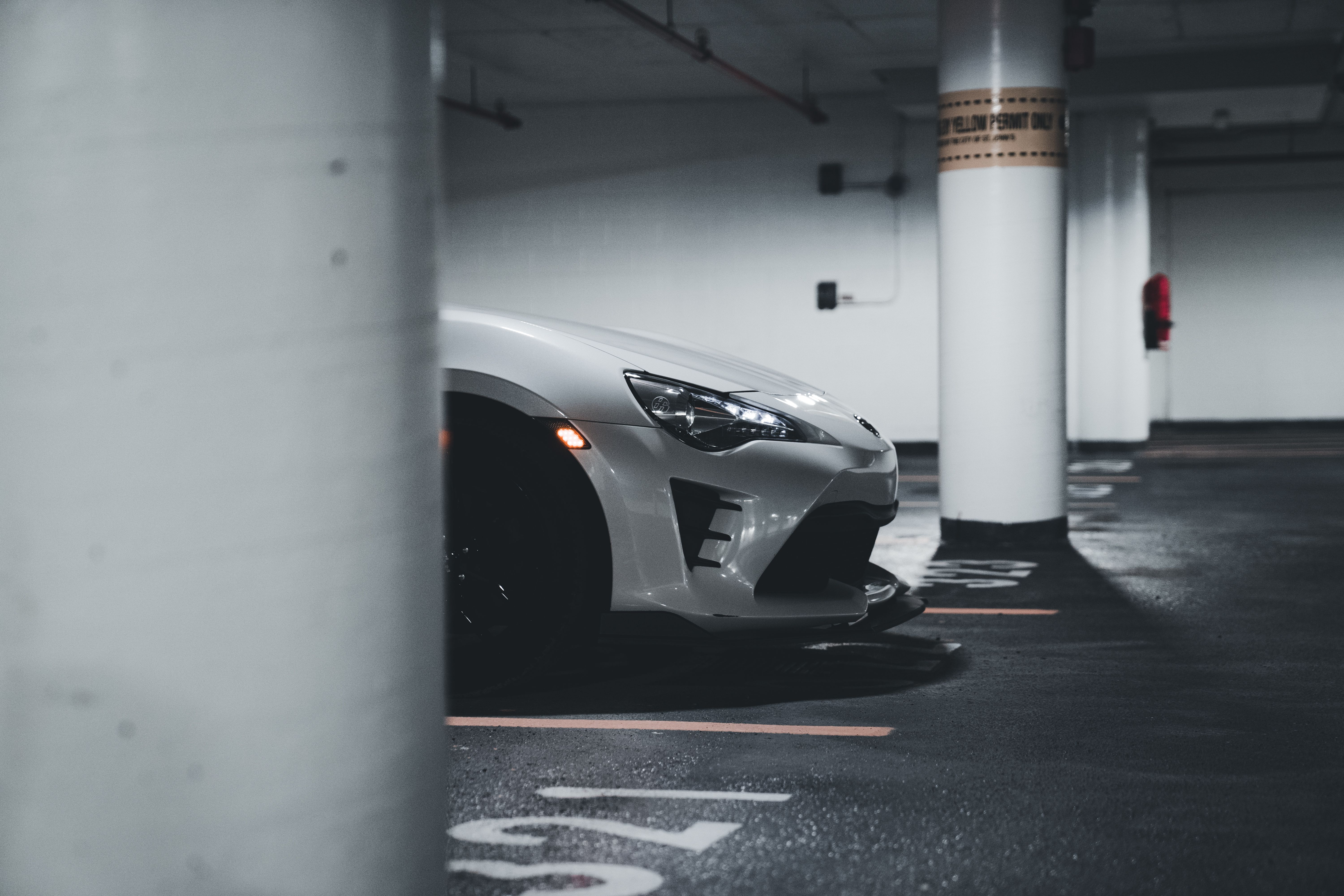 A sleek white sports car partially visible, parked in a dimly lit urban underground garage.