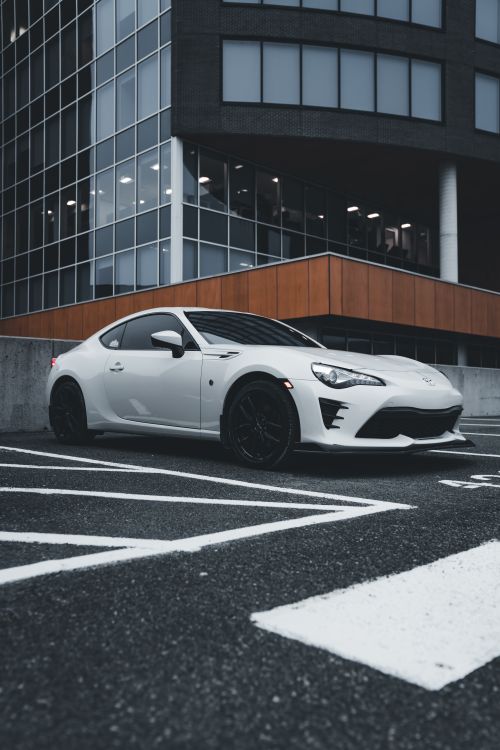 Free A sleek white sports car parked in an urban setting with modern architecture in the background. Stock Photo