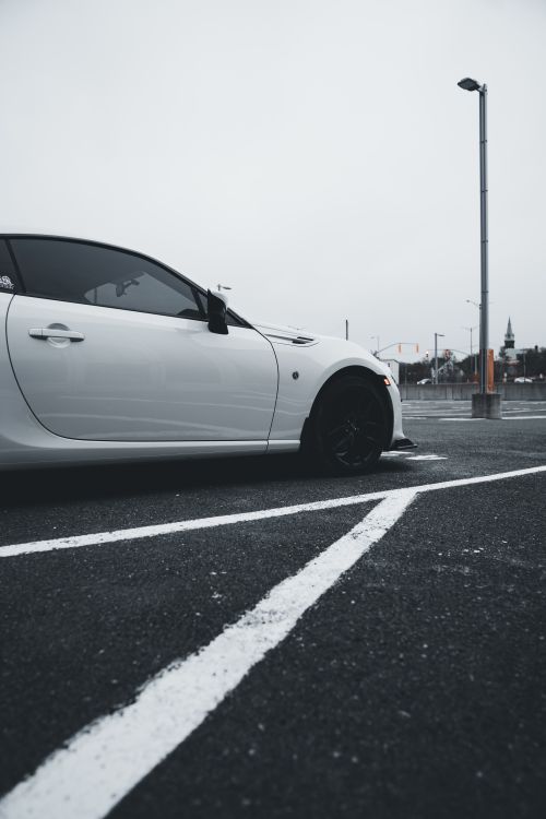 Free A white car parked in an urban parking lot with overcast sky. Stock Photo