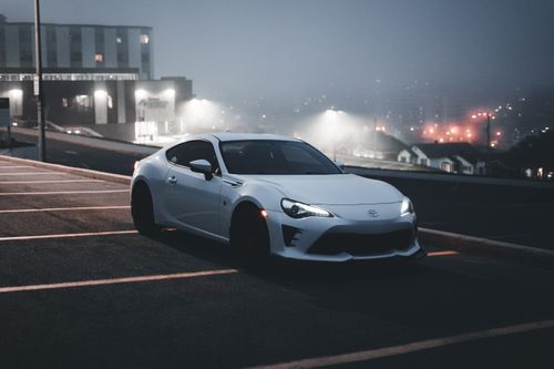 Free A sleek white sports car in a dimly lit urban parking lot at night, exuding a modern and bold vibe. Stock Photo
