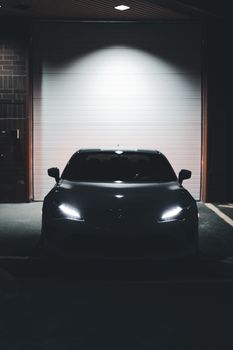 A dark, mysterious car with glowing headlights parked outside a garage at night.