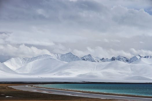 Serene snowy landscape with turquoise waters and majestic mountains beneath a cloudy sky.
