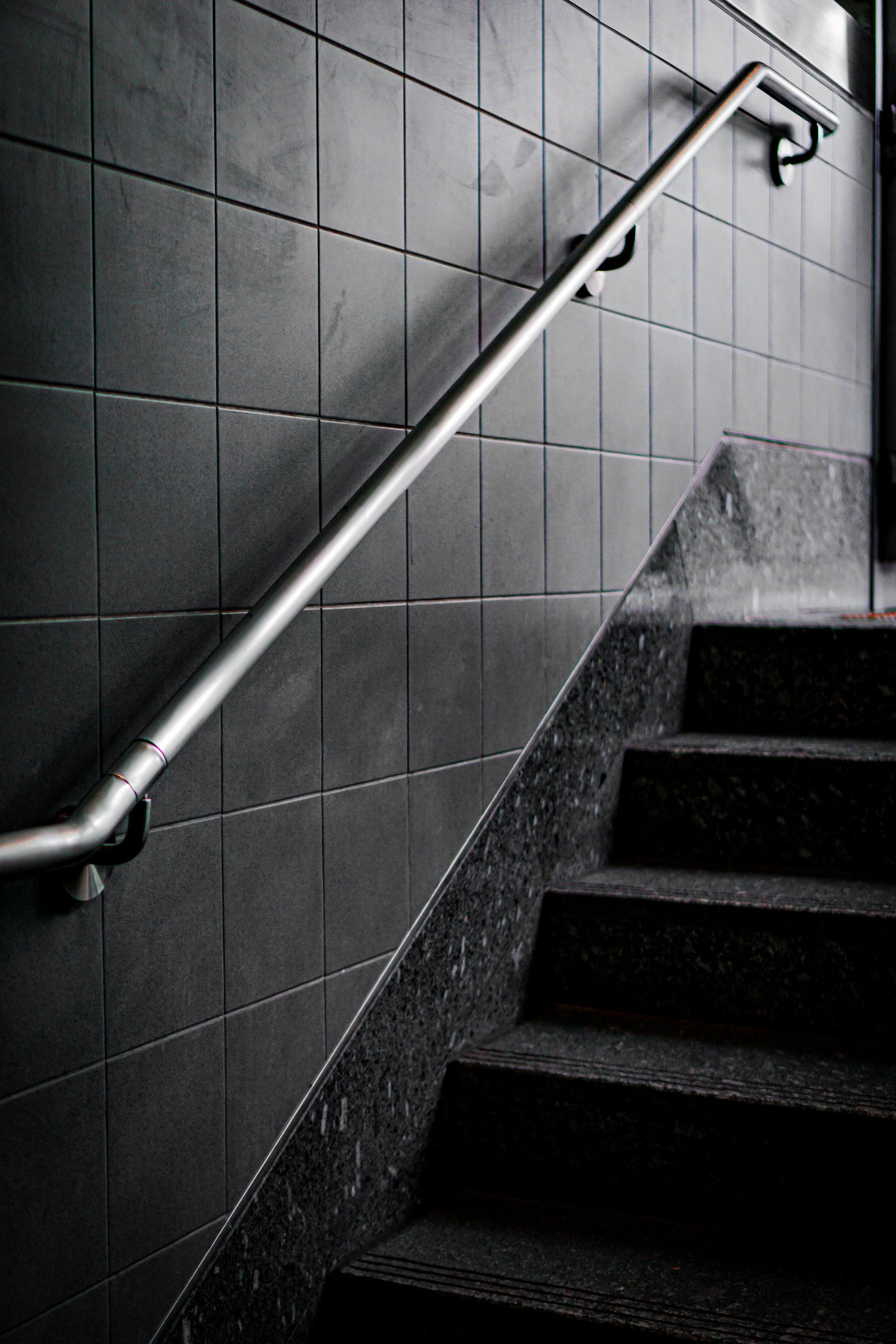 Metal handrail beside dark tiled stairs