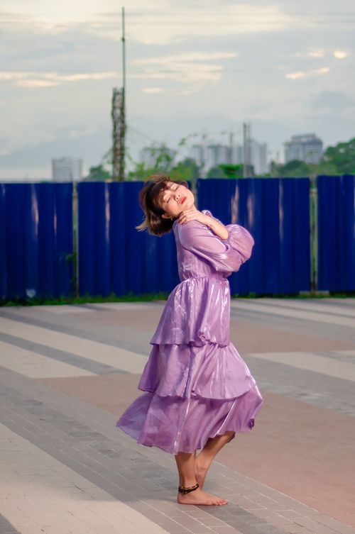 Free A fashionable woman in a purple dress poses gracefully in an urban outdoor setting during the day. Stock Photo