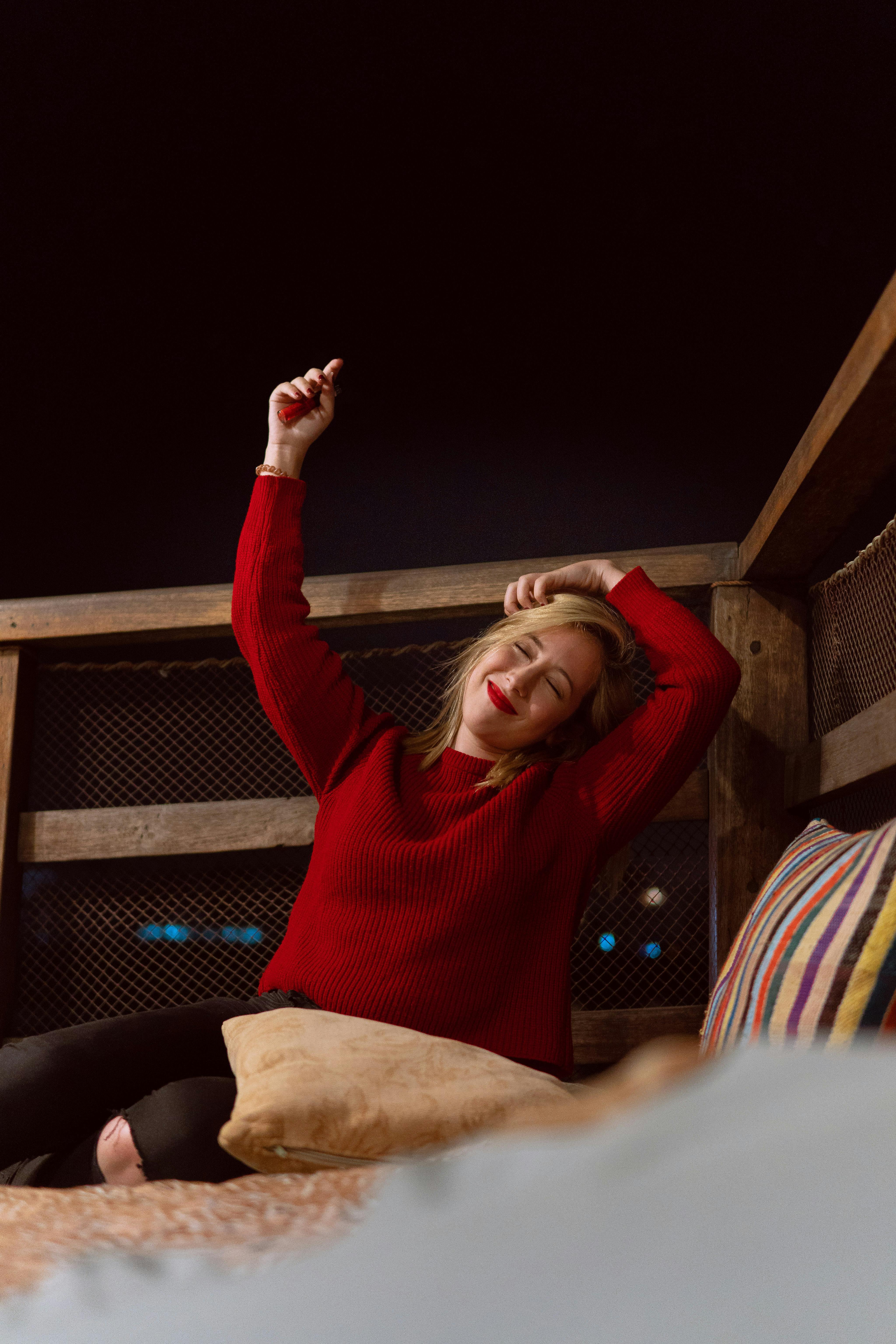 A woman in a red sweater enjoys a relaxing night outdoors on a rooftop with pillows.