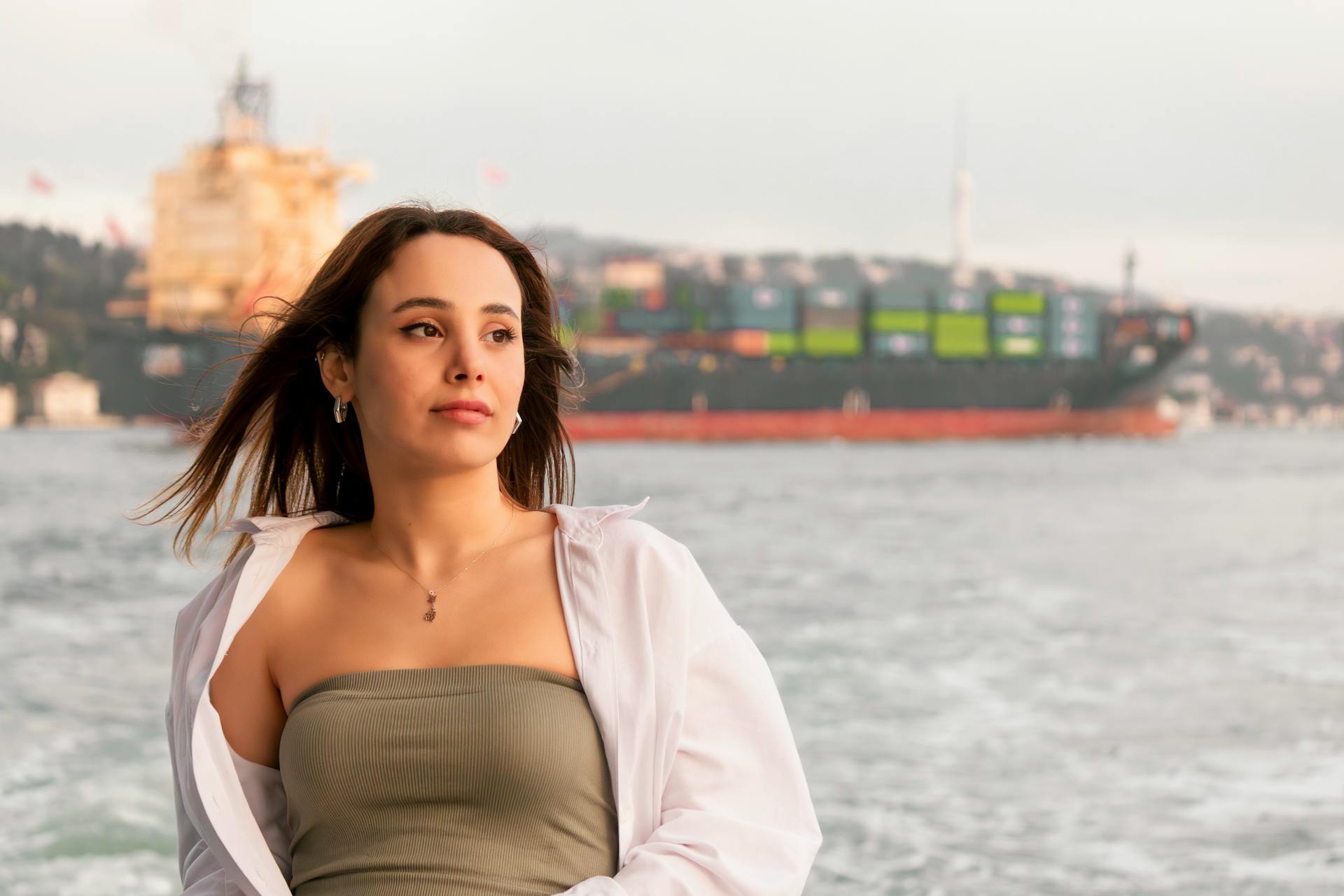 A woman stands confidently by the sea with a container ship in the background. Perfect for travel or lifestyle themes.
