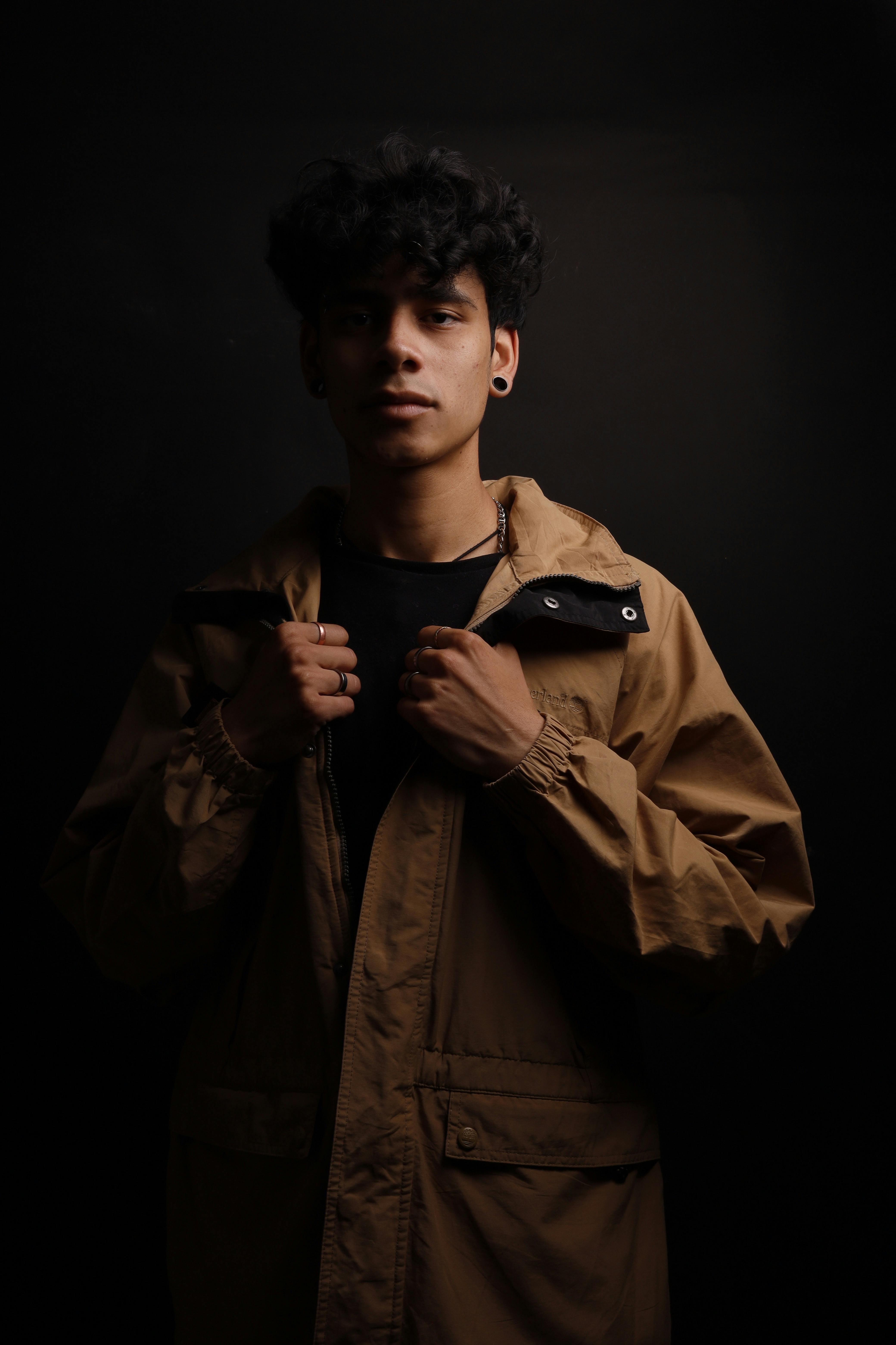 Portrait of a stylish young man in a brown jacket against a dark background, showcasing modern fashion.