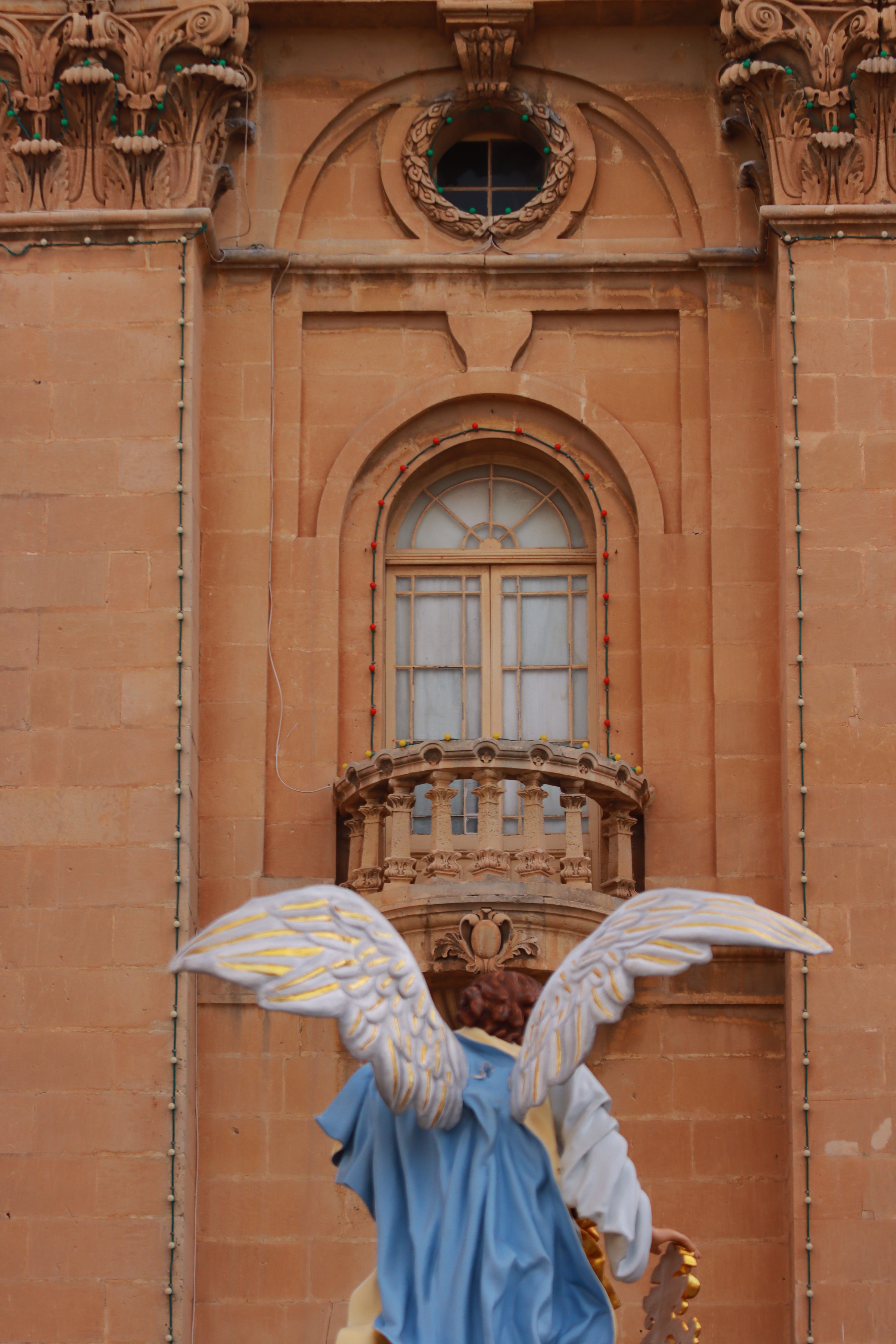 A stunning angel sculpture stands before a historic balcony in Valletta, Malta.