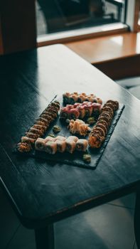 Tastefully arranged sushi rolls on a slate tray, beautifully presented in a dimly lit restaurant setting.