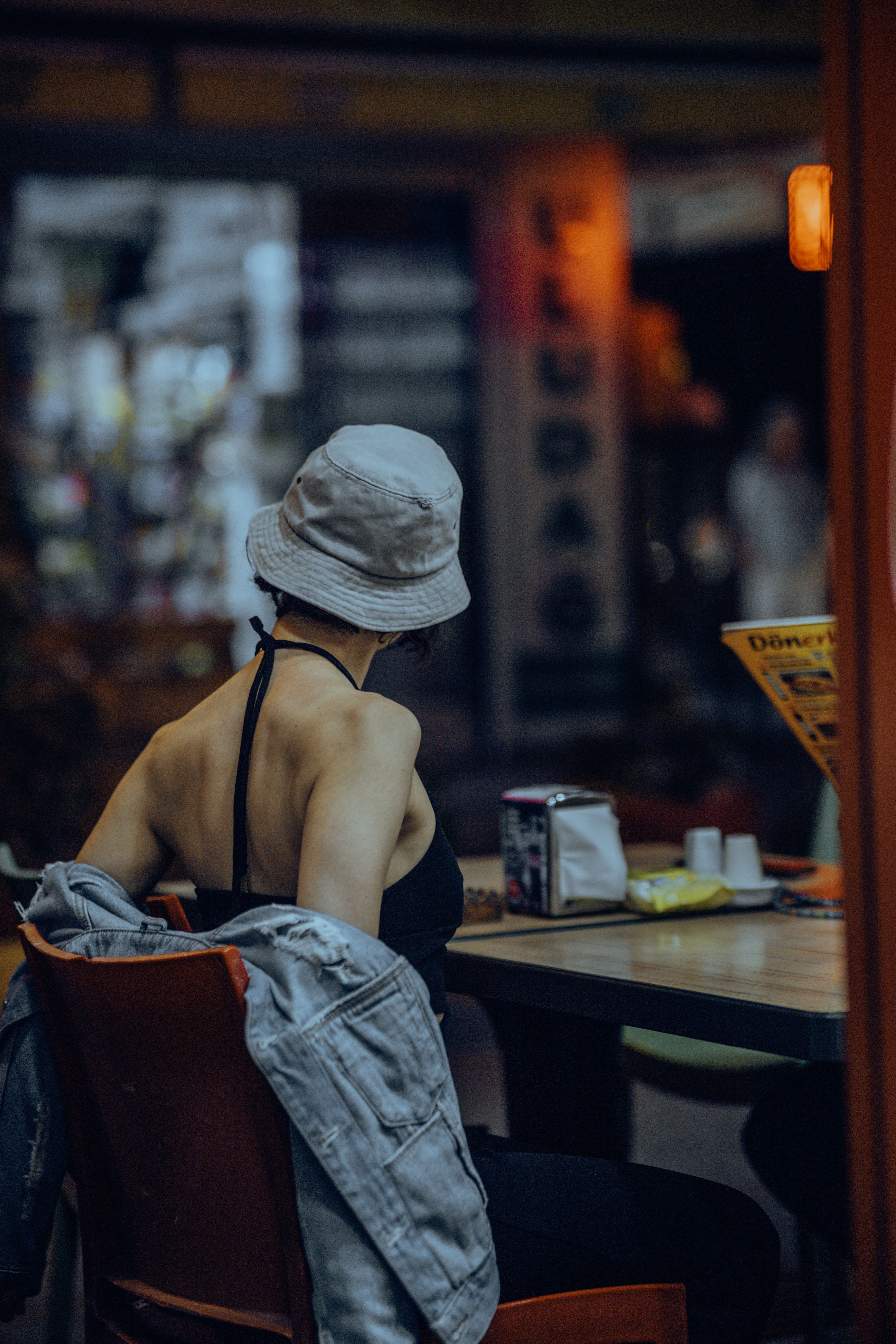 A fashionable woman wearing a bucket hat and black top relaxes indoors, creating a candid urban lifestyle scene.