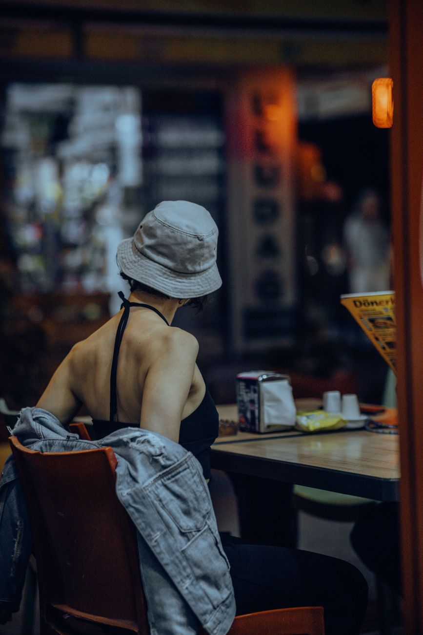 A fashionable woman wearing a bucket hat and black top relaxes indoors, creating a candid urban lifestyle scene.