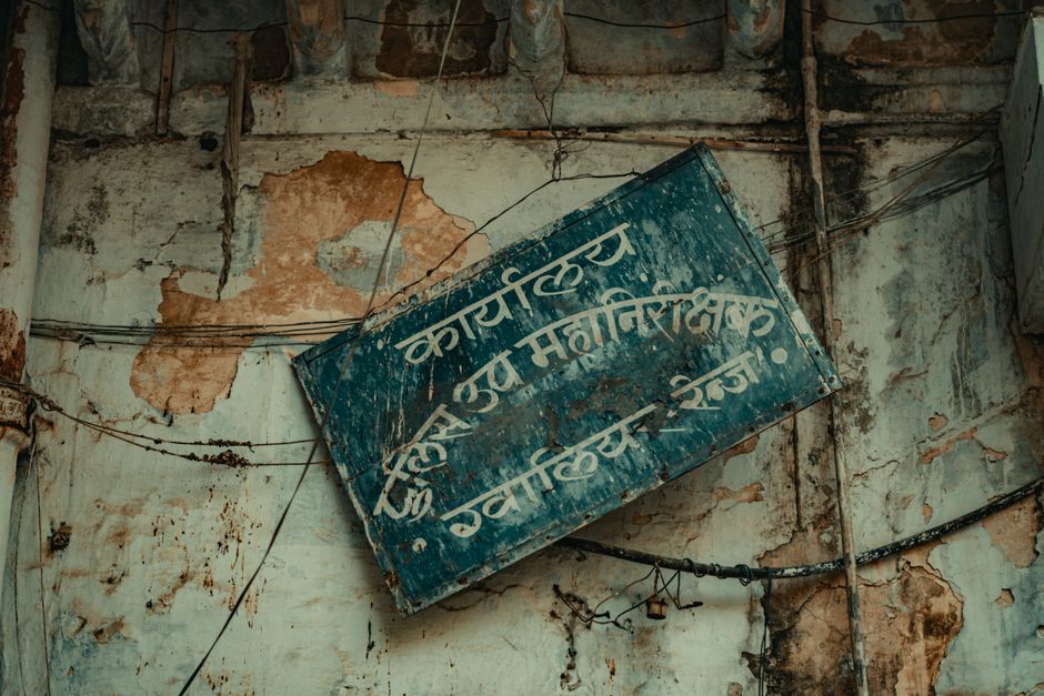Aged and decaying wall with a rusty sign in Hindi script, showcasing urban decay.
