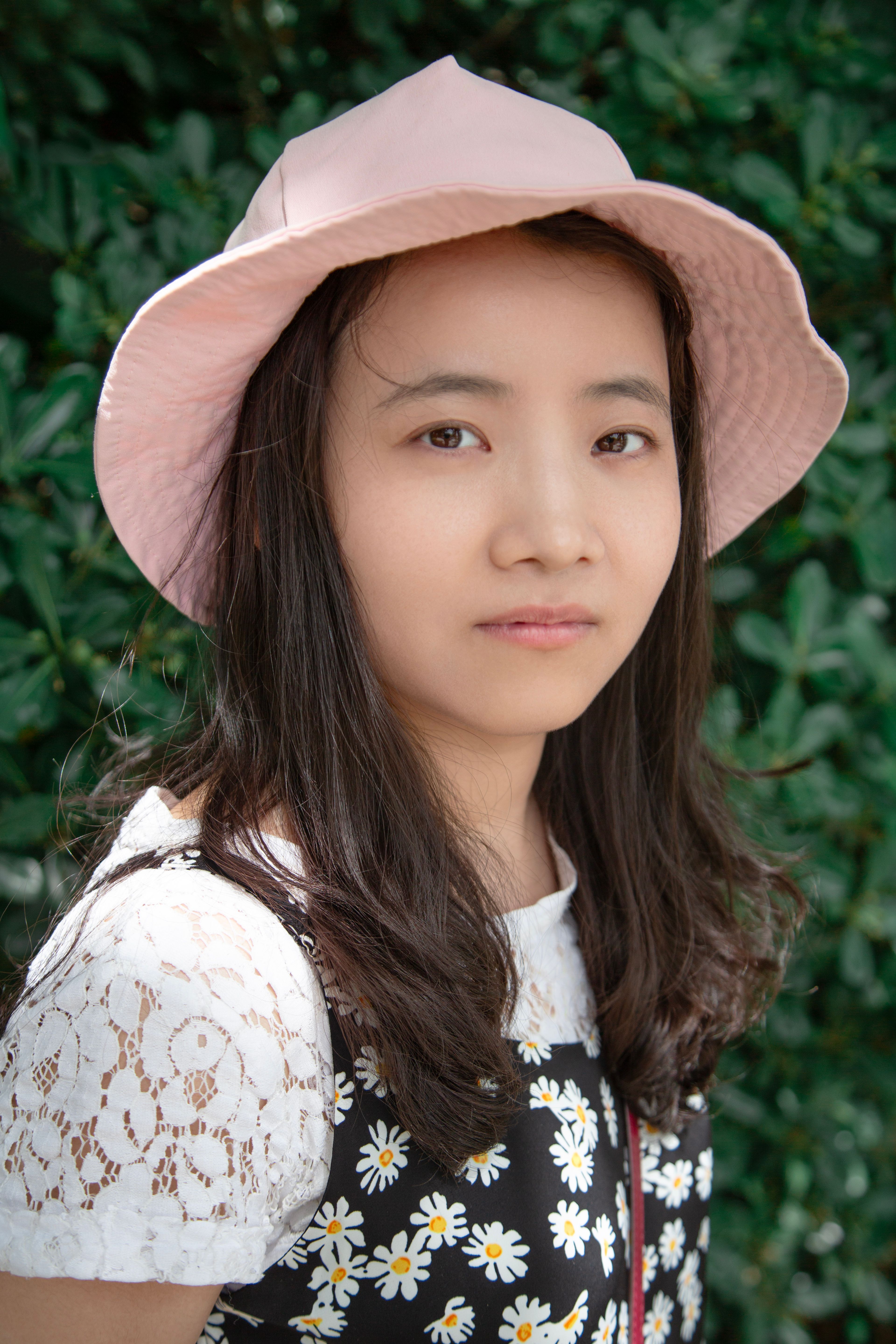 Portrait of a young woman outdoors in a floral dress and pink hat, embracing summer style.
