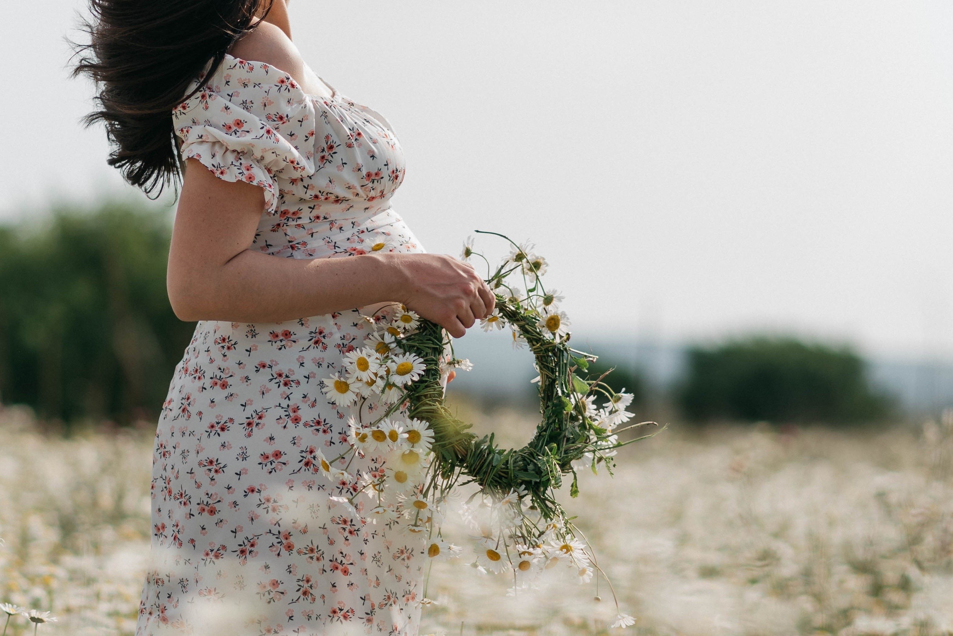 Pregnant woman in meadow holding a blossoming wreath, evoking a serene spring atmosphere.