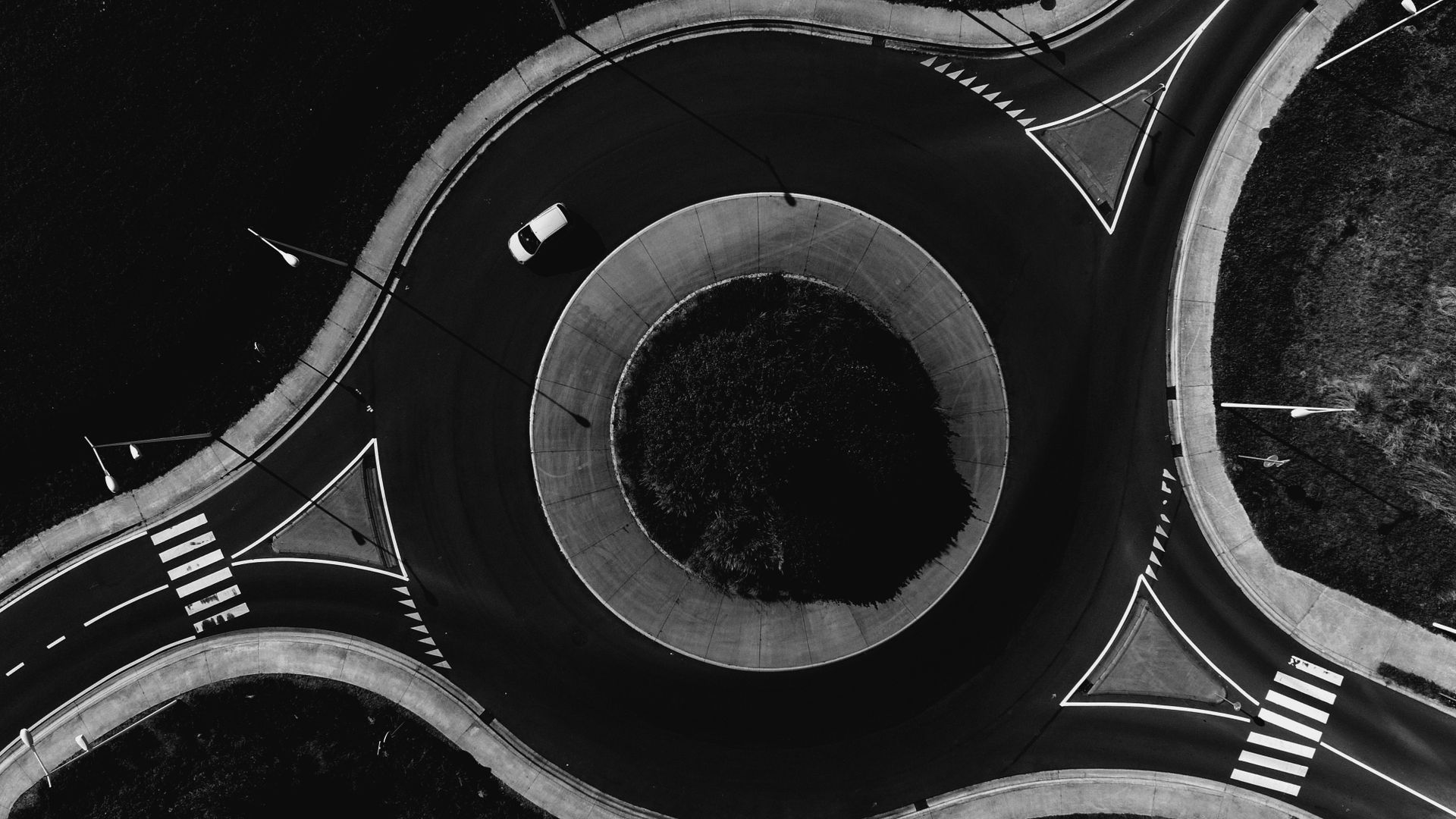 Monochrome aerial view of a modern traffic roundabout with a single car navigating the circle.